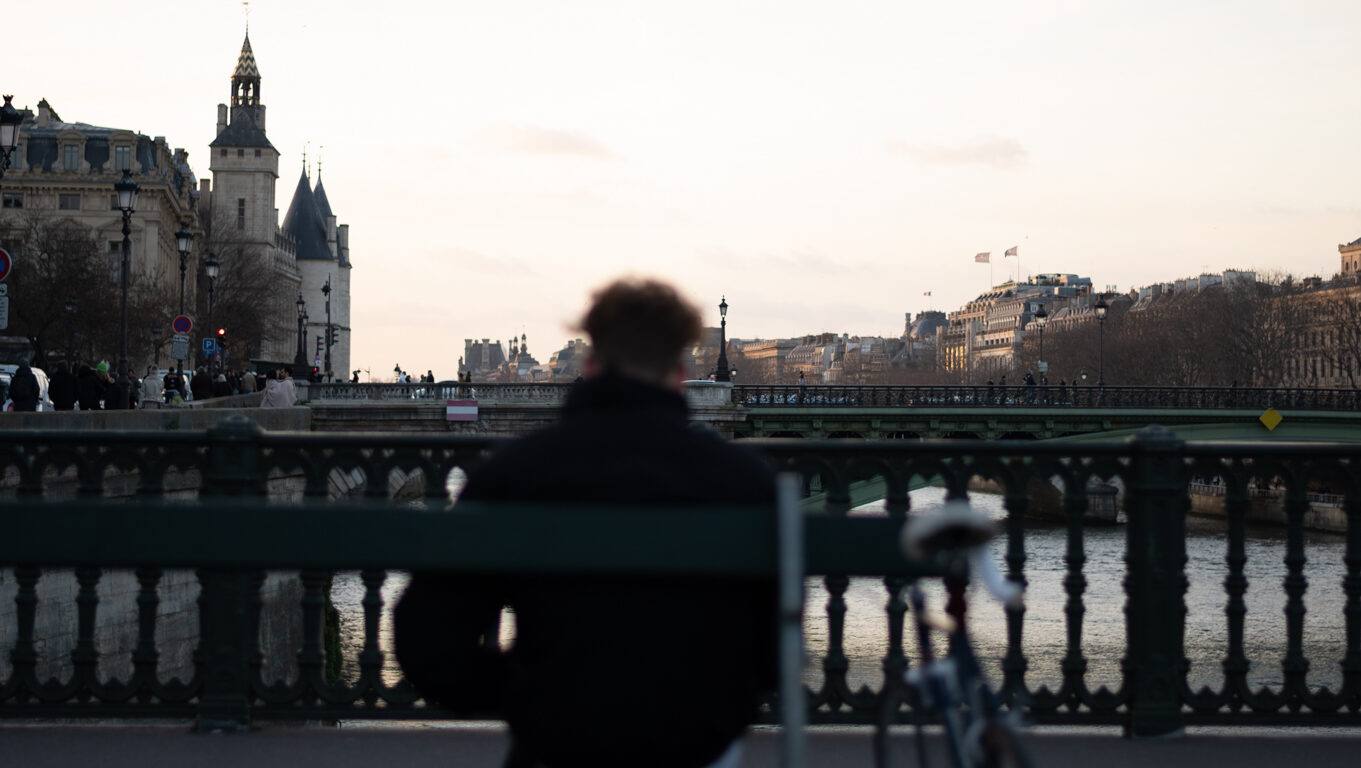 A cyclist rests on a bench and enjoys the view on the Seine.