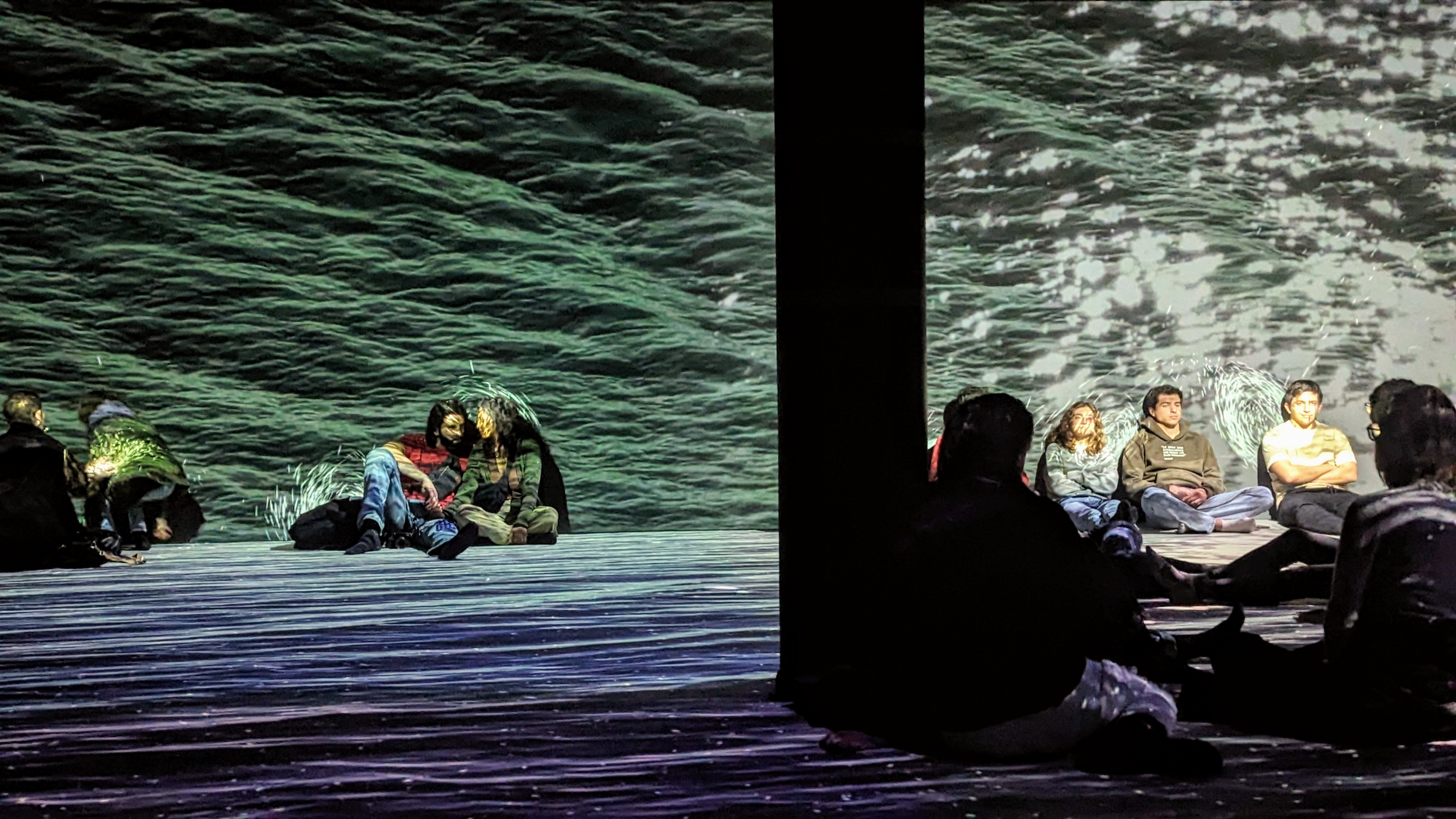 Visitors of the "En amour" experience at the Philharmonie in Paris are sitting on the floor, taking in the visuals and music.