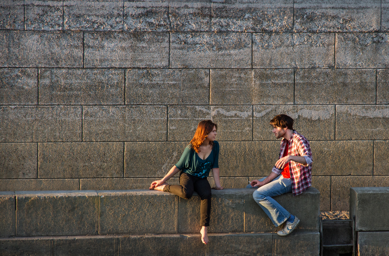 A young woman and a young man are sitting on the banks of the Seine river in Paris, practicing their French language skills.