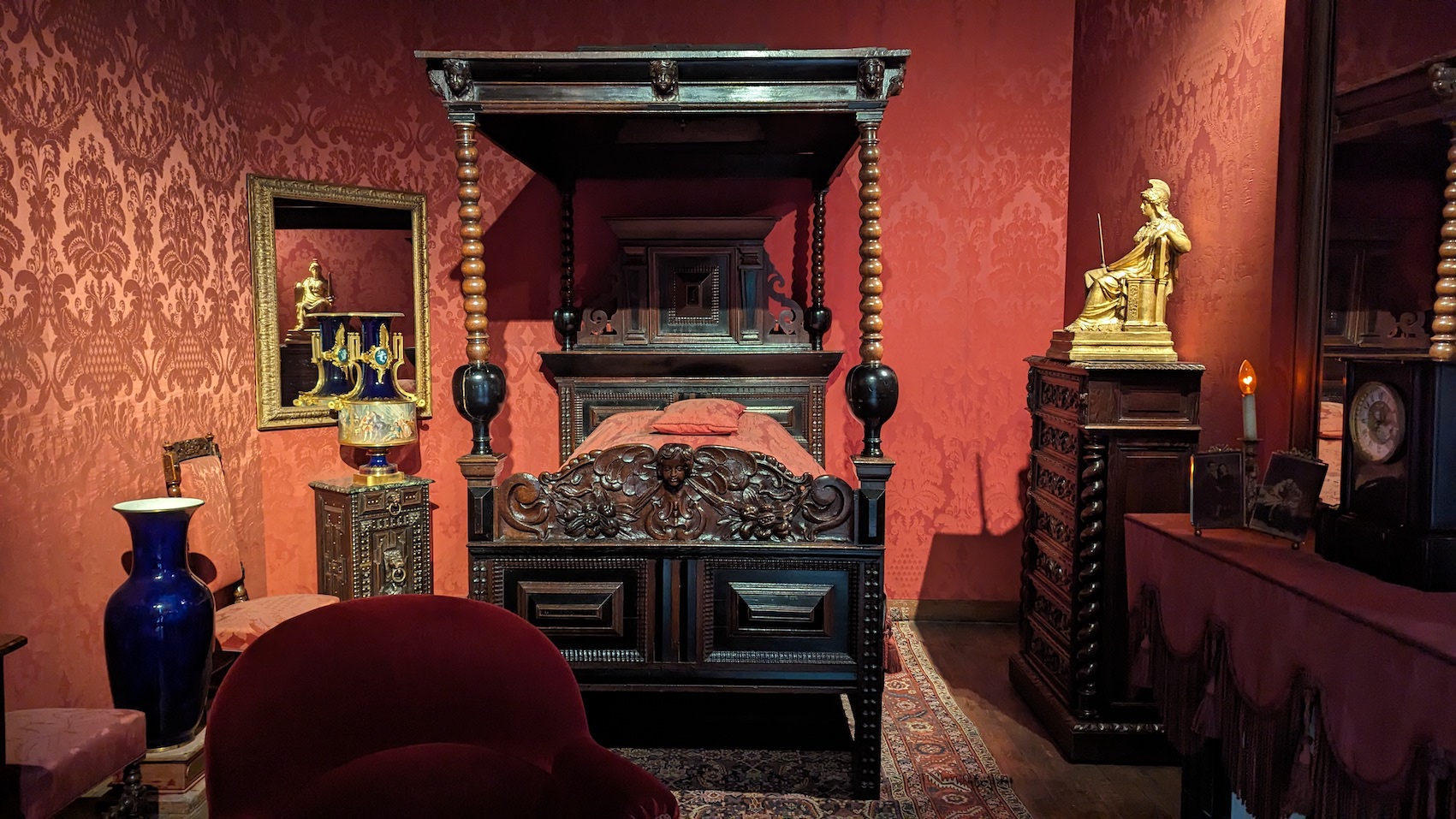 The famous French writer Victor Hugo's bedroom in his former apartment at Place des Vosges with red tapestry and a dark wooden four-poster bed.