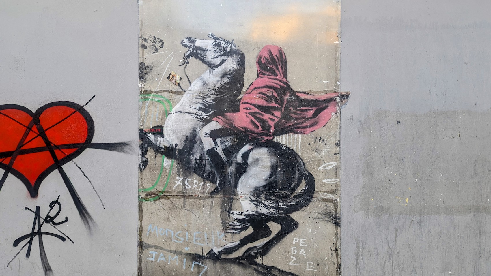 Banksy's the Red Horseman - a cavalier with a red scarf that hides his face on a white horse - on a wall in northeaster Paris, next to other graffiti.